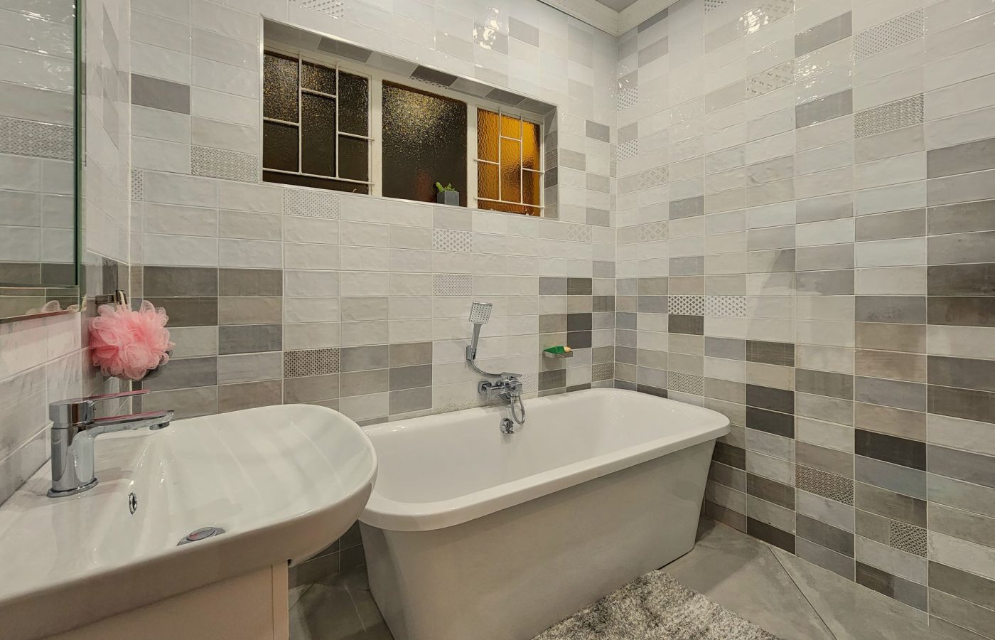 Badezimmer mit Wandfliesen in verschiedenen Formaten und Grautönen